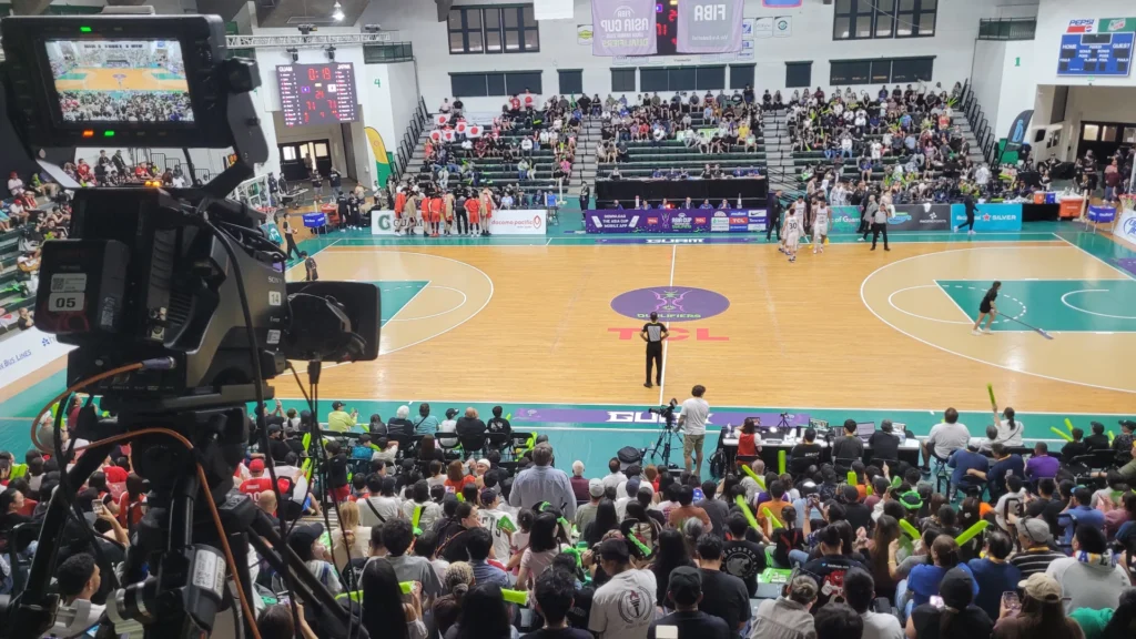 A professional video camera positioned in a basketball arena filled with spectators, showcasing a live sports event